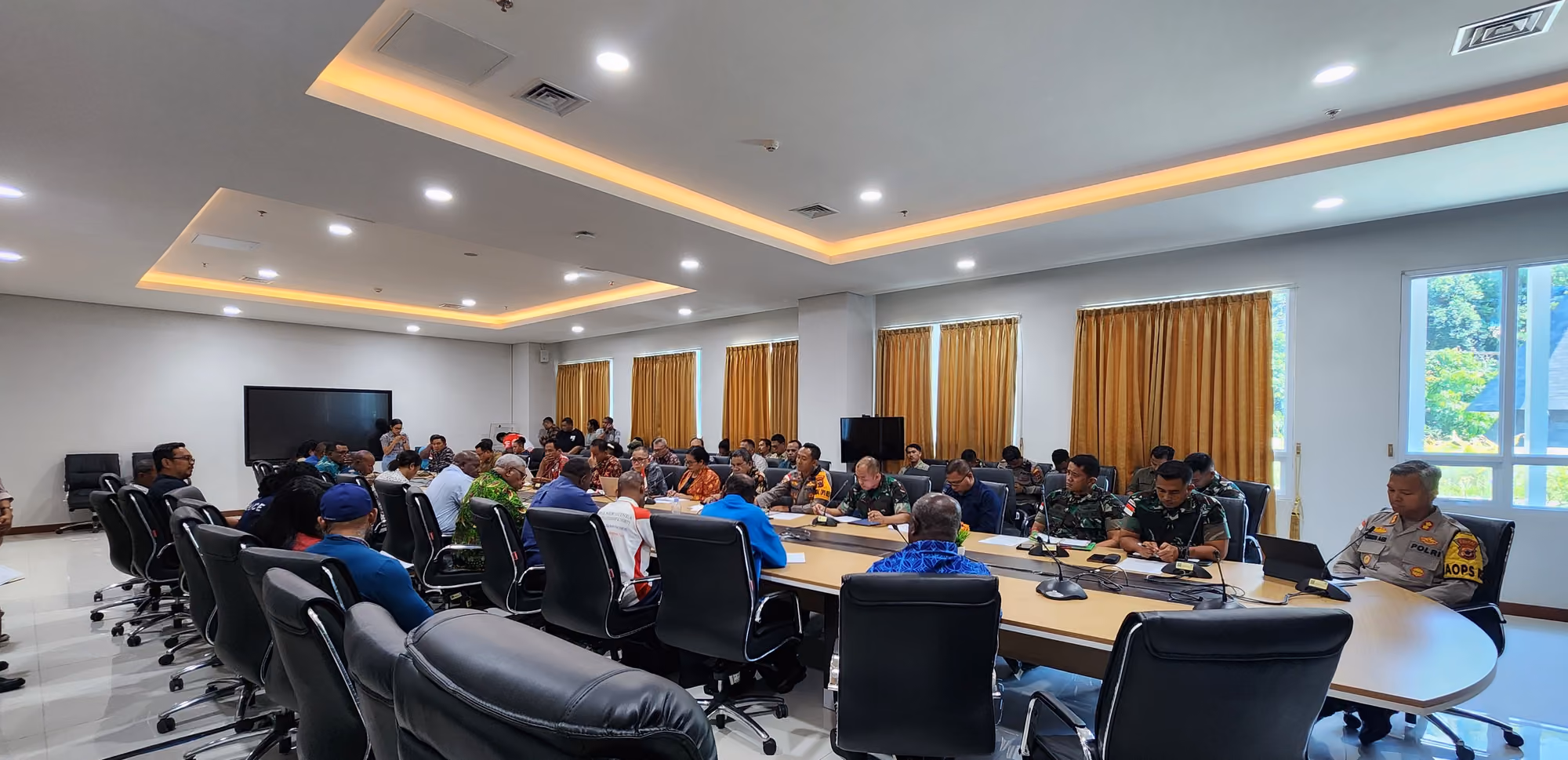 Ruang rapat tertata dengan meja panjang berbentuk persegi dan peserta yang mengikuti kegiatan.