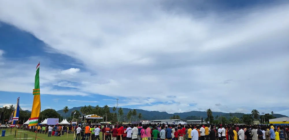 Area acara di lapangan terbuka dipenuhi peserta dengan latar perbukitan hijau.