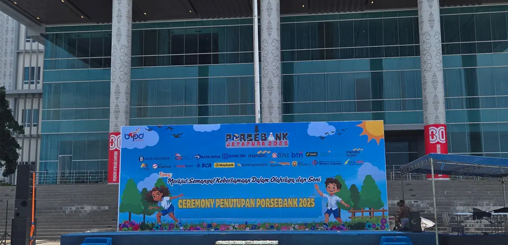 Backdrop biru berukuran besar terpasang di halaman gedung berpilar pada siang hari.