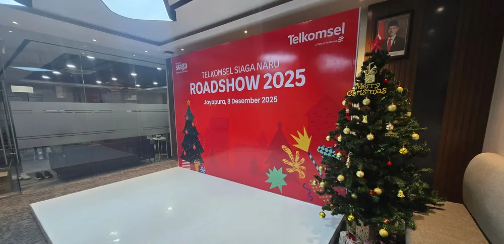 Backdrop acara berwarna merah dan pohon Natal berhias tertata di ruang acara dalam gedung.
