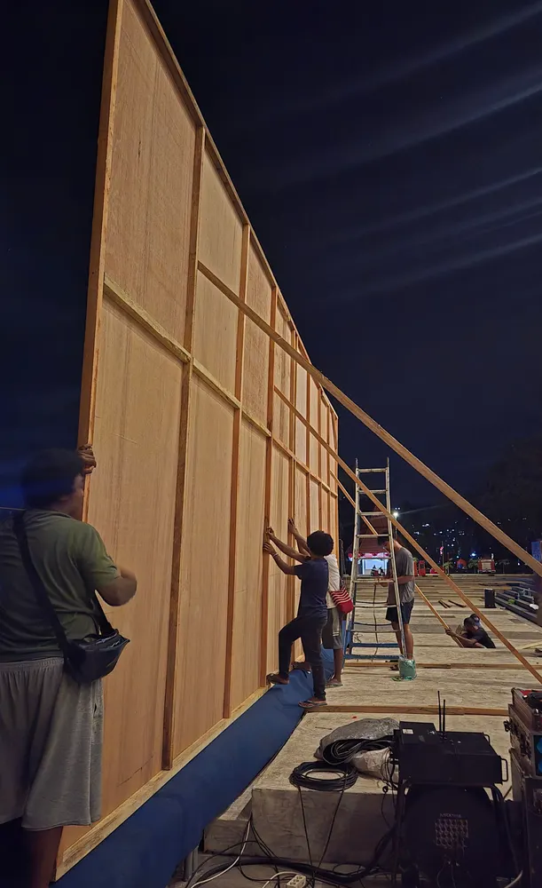 Kru memasang dinding backdrop kayu berukuran besar menggunakan tangga.
