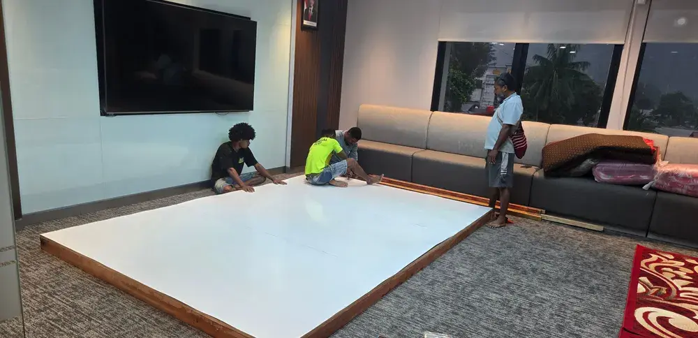 Kru merakit panel panggung rendah berpermukaan putih di dalam ruangan dengan peralatan kerja di sekelilingnya.