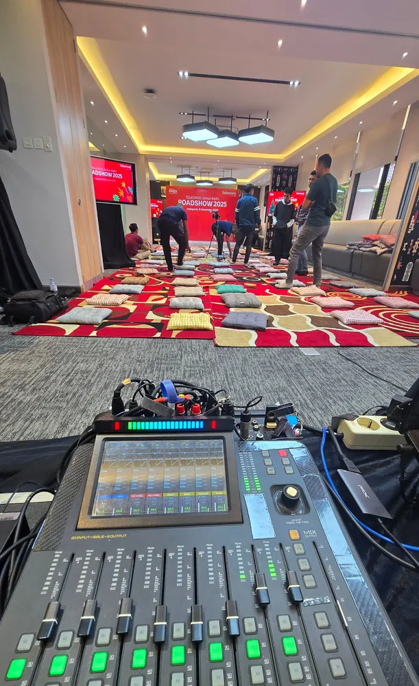 Konsol pengendali audio dengan deretan kanal dan layar di posisi operator selama acara.