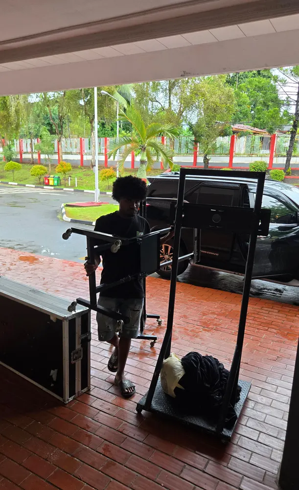 Kru membawa peti peralatan produksi melewati area luar gedung.