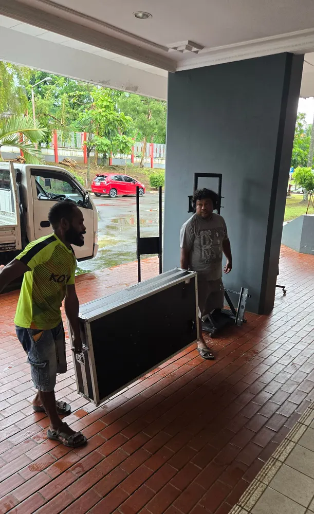 Kru memindahkan peti peralatan menggunakan troli menuju area acara di dalam gedung.