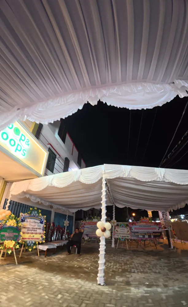 Langit-langit tenda berkain putih bergelombang dengan lampu dan dekorasi pada acara malam hari.