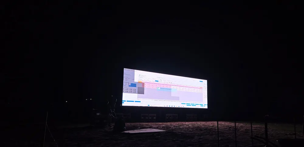 Layar LED berukuran besar menyala pada malam hari di area lapangan terbuka.