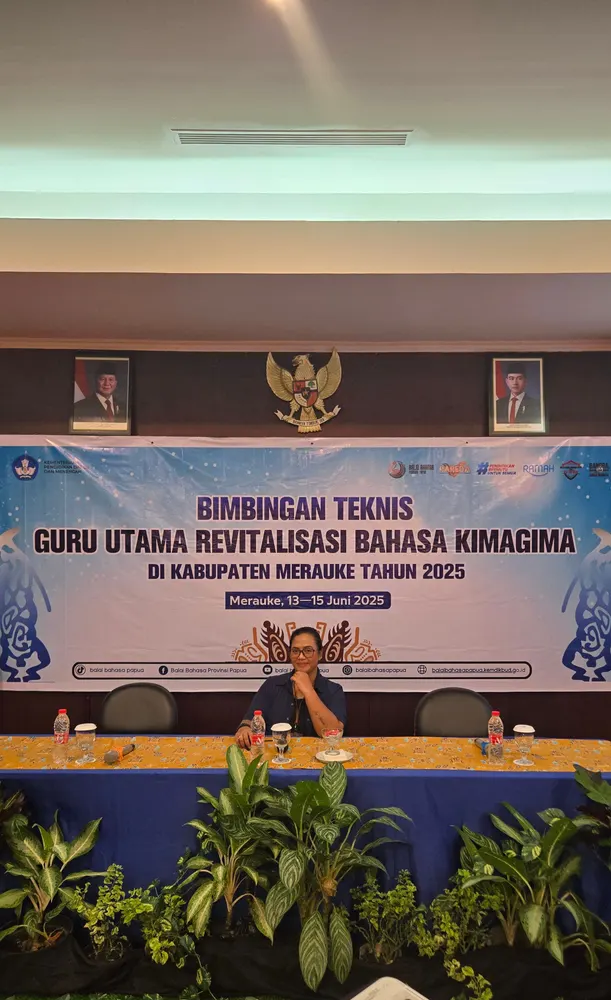 Meja panel tertata di depan backdrop kegiatan pemerintah daerah di dalam ruangan.