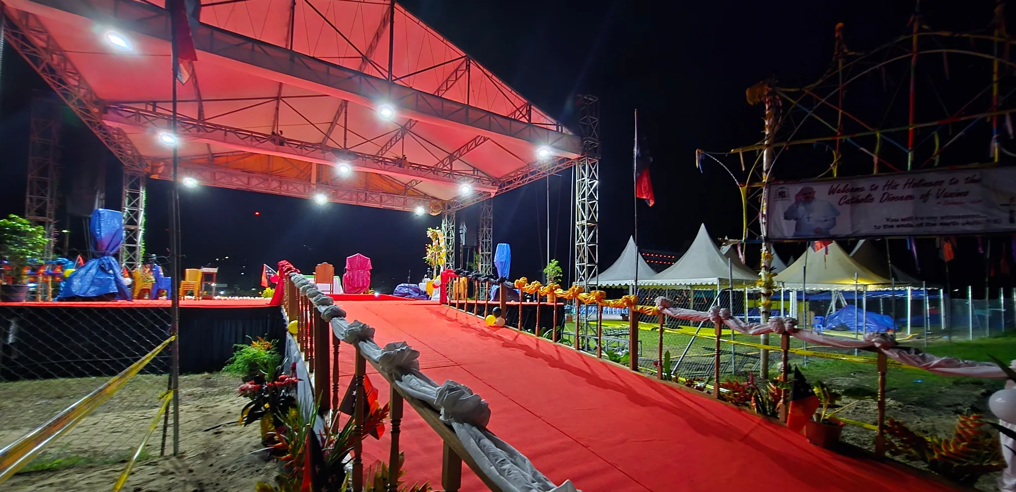 Area panggung berkarpet merah memanjang dengan rangka lampu di kedua sisi dan tenda peserta di sekelilingnya.