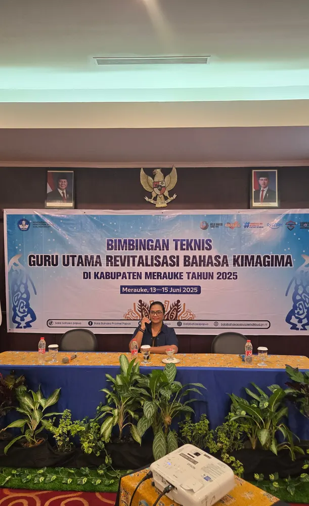 Panggung kegiatan pemerintah dengan backdrop, meja panel, dan tanaman hias.
