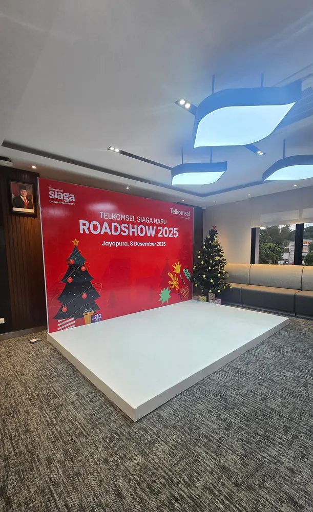 Panggung rendah berlapis putih dengan backdrop merah bertuliskan “Telkomsel Siaga NARU Roadshow 2025” di ruang acara.