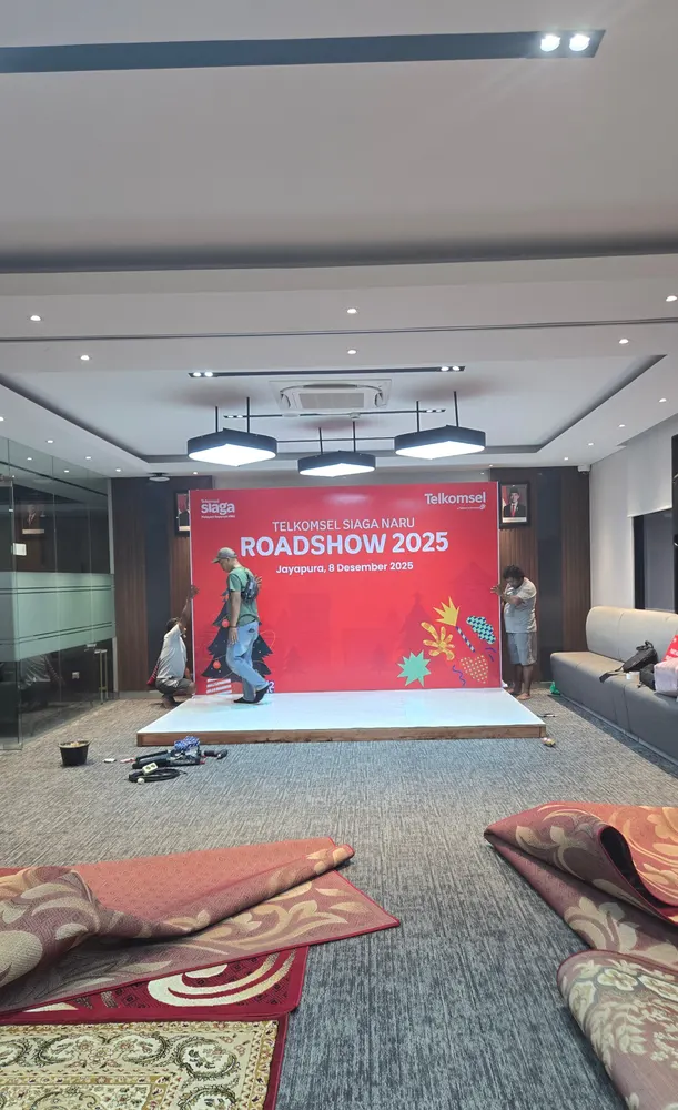Kru membentangkan backdrop merah berukuran besar di lantai ruang acara dalam gedung.