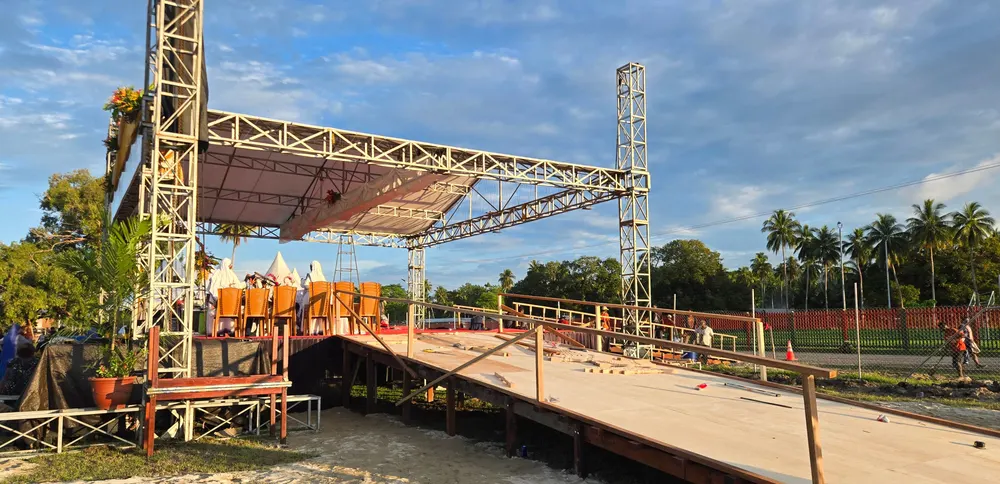 Rangka baja panggung dan lantai kayu dalam proses pemasangan di lapangan terbuka pada siang hari.