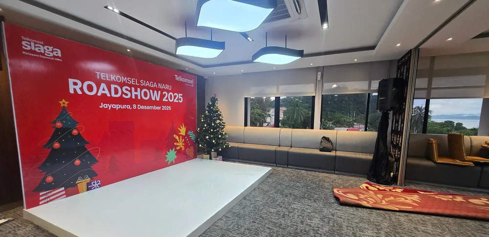 Ruang acara dalam gedung dengan backdrop merah dan panggung rendah yang telah tertata.
