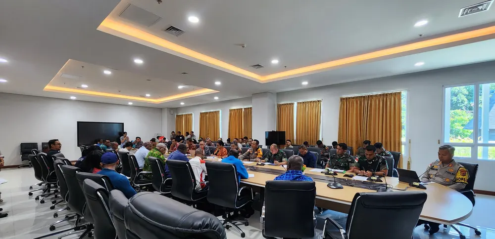 Ruang rapat tertata dengan meja panjang berbentuk persegi dan peserta yang mengikuti kegiatan.