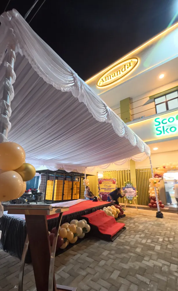 Tenda berkain putih dengan dekorasi balon berdiri di depan gerai untuk acara peresmian.