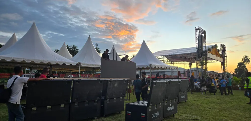 Tenda acara dan peti peralatan tertata di lapangan saat matahari terbenam.