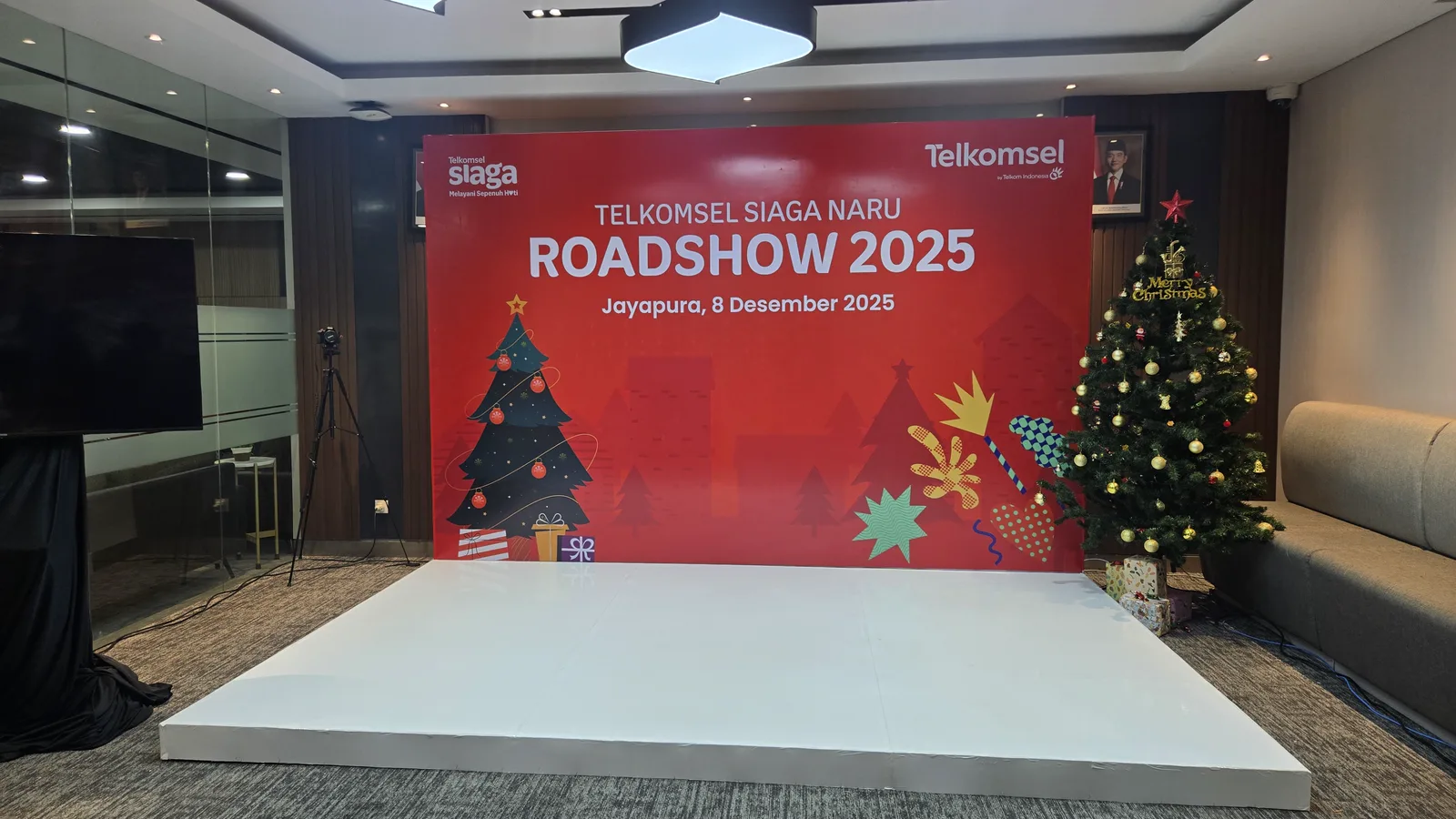 Panggung Telkomsel Siaga NARU Roadshow 2025 di Jayapura dengan backdrop merah, layar display, dan dekorasi pohon Natal.
